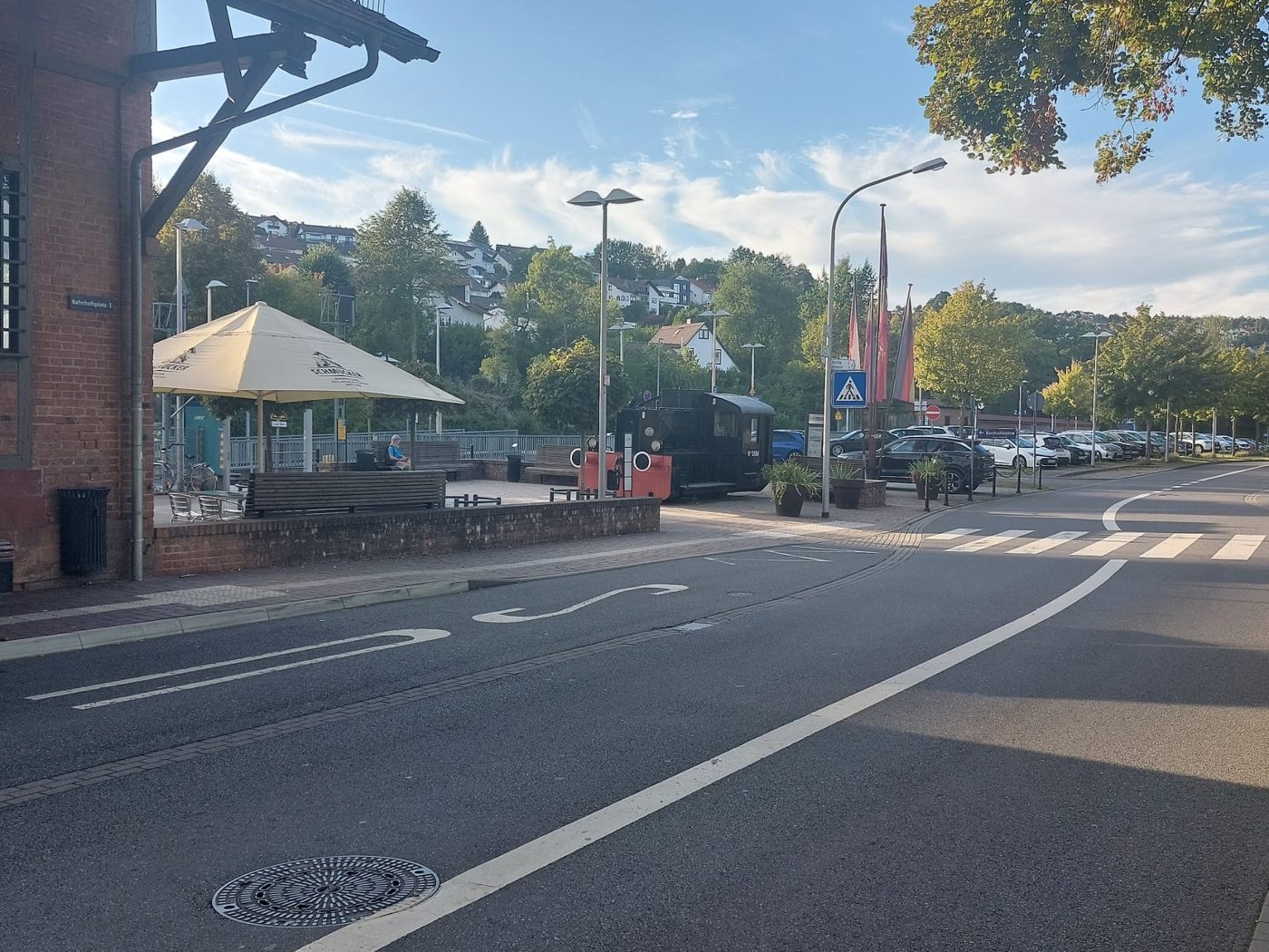 Bahnhofplatz 1 in Erbach mit Backsteingebäude, Sonnenschirm, Bänken und historischer Lok