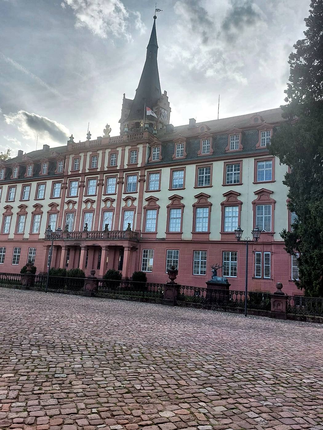 Fassade von Schloss Erbach im Odenwald mit dem Bergfried, bronzener Hirschfigur am Zaun und Kopfsteinpflaster im Vordergrund